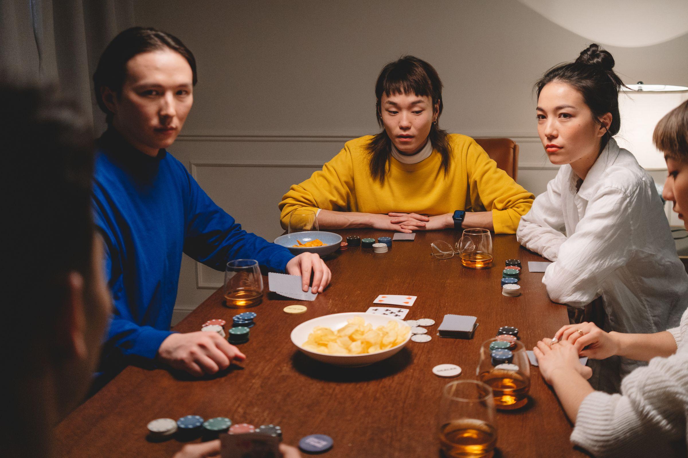 Friends playing poker around a wooden table at home, with chips, cards and drinks in front of them